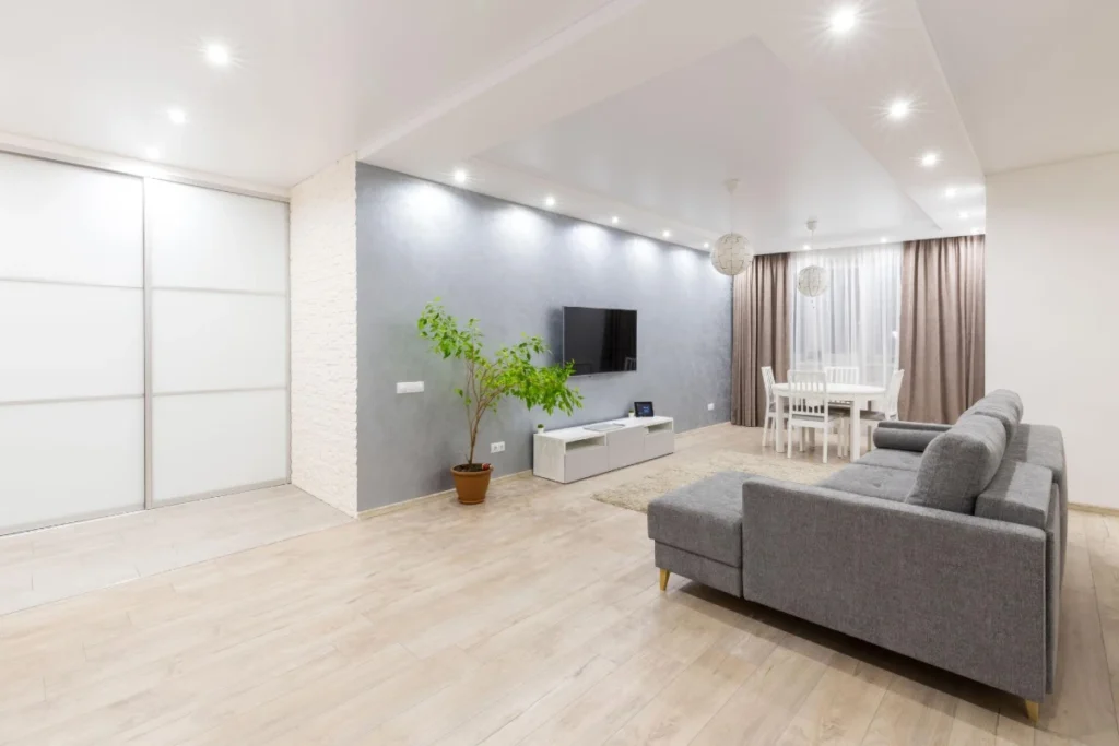 Minimalistički uređen dnevni boravak sa belim ugradnim plakarom za skriveno odlaganje, svetlim podom i čistim linijama nameštaja.